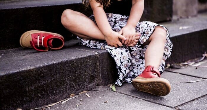Little girl sitting on a step taking off her red shoes