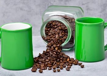 Coffee beans pouring from glass jar with two mugs on each side
