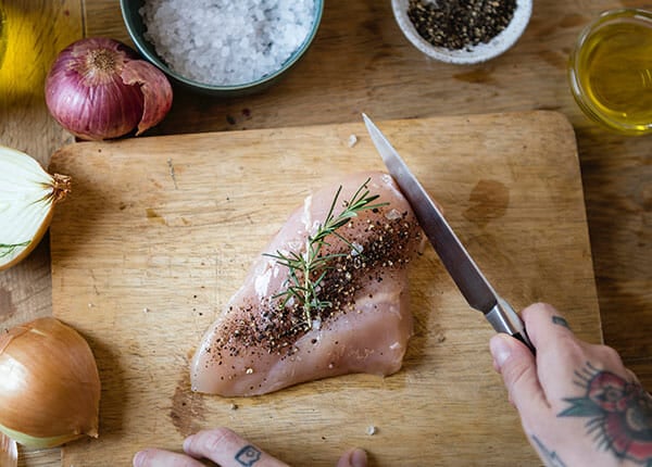 A person slicing raw chicken meat