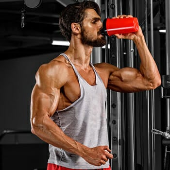 A muscular man drinking creatine at the gym