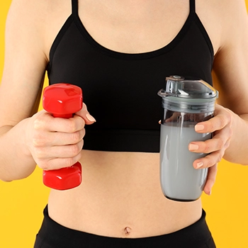 Holding a dumbbell and a tumbler with pre workout drink
