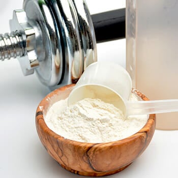 Close up shot of a scoop of BCAA on a wooden bowl with a dumbbell on the side