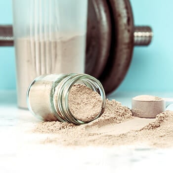 A glass jar of protein powder spilled on a table