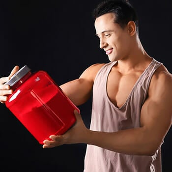 A muscular man holding a tub of whey protein