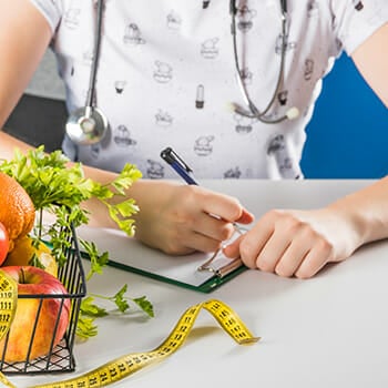 A woman writing down on a clipboard beside a basket of fruits