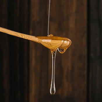 Close up shot of honey dripping onto a wooden spoon