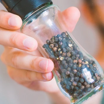A person holding a jar of whole peppercorns