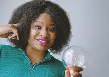 A person holding a lightbulb and pointing to her head