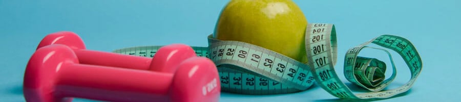 pink dumbbells, a measuring tape and a green apple