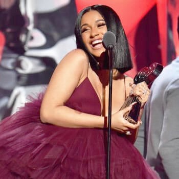 cardi b wearing a maroon gown while holding an award