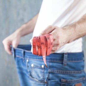 man holding up his loose pants while showing a measuring tape