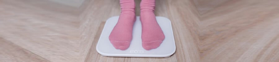 woman with pink socks stepping on a weighing scale