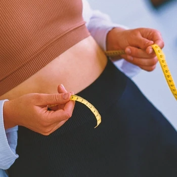 A woman measuring her waist using a measuring tape