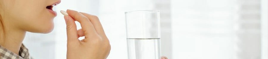 woman taking a pill to her mouth while holding a glass of water