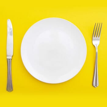 white plate, fork and knife in a yellow background