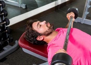man laying down in a gym bench while lifting a barbell
