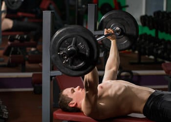 man using a barbell laying down on a bench