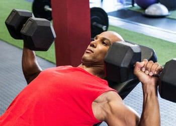 man in an incline bench working out using dumbbells