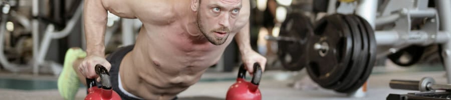 shirtless man using kettlebells while doing push ups