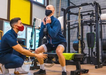 instructor teaching a man how to squat in a gym