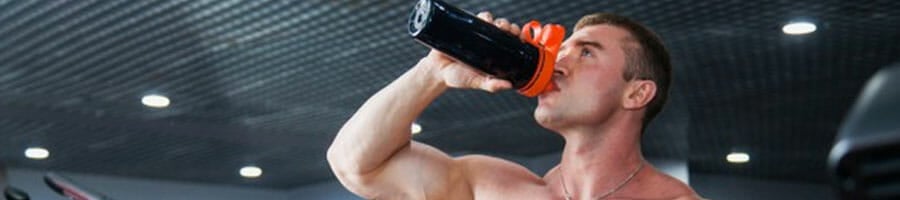 shirtless man drinking supplements in the gym