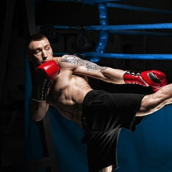 shirtless man kicking a punching bag in the gym