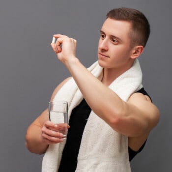 man in gym clothes holding up a piece of pill and a glass of water