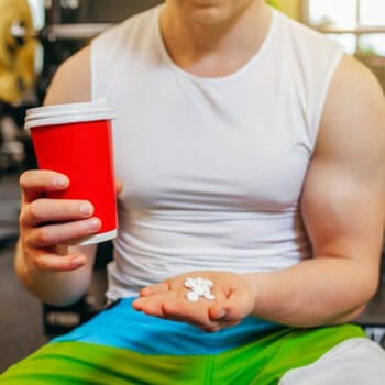 man holding pills and a cup in a gym
