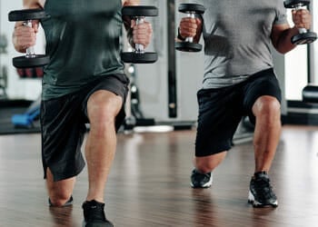 two men doing lunges while holding a dumbbell