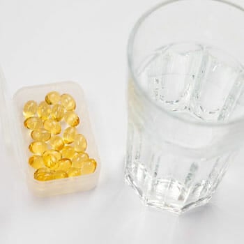 yellow pills in a container with a water in a glass