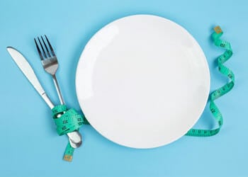 empty plate with spoon and fork with a measuring tape wrapped on it