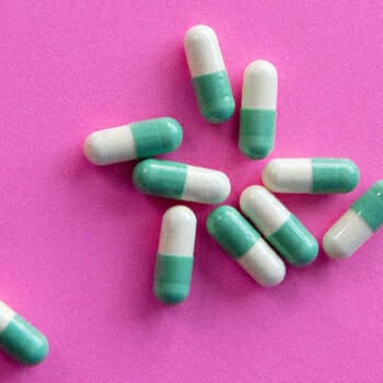 Green and white pills on a pink platform