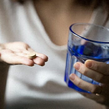 A person holding a pill and a water on the other hand