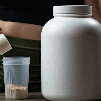 A big container of a powdered supplement and a girl pouring it to a small container