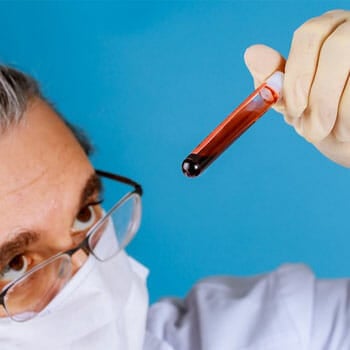 medical person looking raising and looking closely through a blood vial