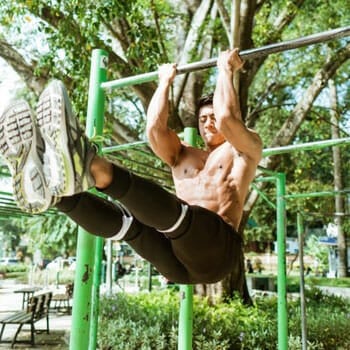 shirtless man using a bar at a park to do pullups