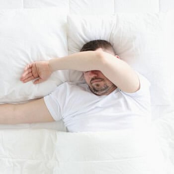 man sleeping on a bed with his arms covering his eyes