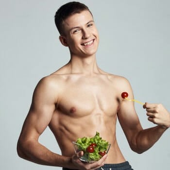 shirtless man holding up a bowl filled with salad