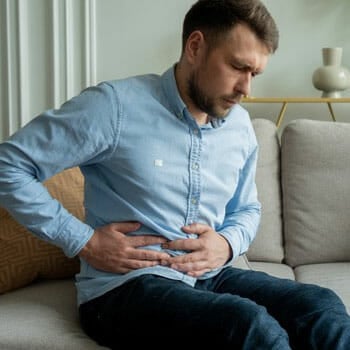 man seated down holding his bellyache