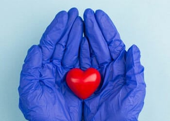 hands in surgical gloves holding a small heart toy