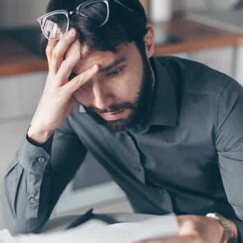 man holding his head in worry while reading a paper