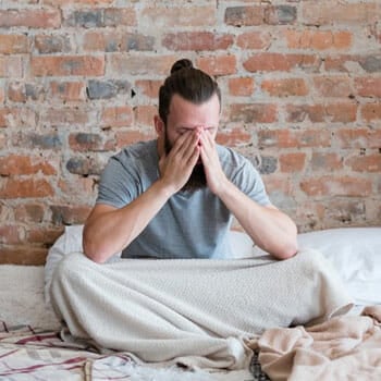 man struggling to sleep seated on bed