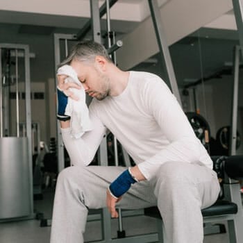 man resting in a gym while wiping sweat