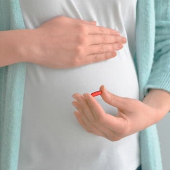 woman with a pregnant belly holding her stomach and a capsule