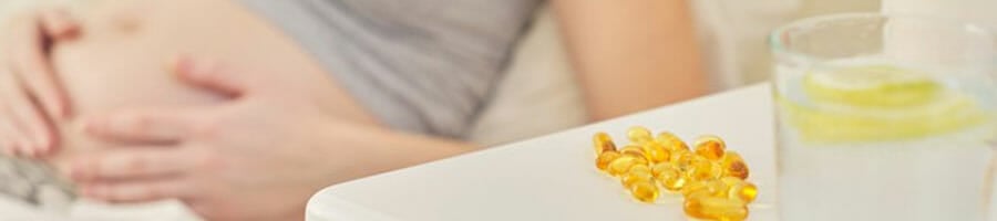 woman holding her pregnancy belly, with fish oils displayed on her bed side table