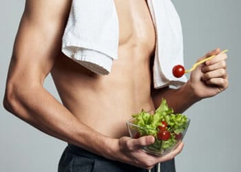 man eating a salad bowl shirtless