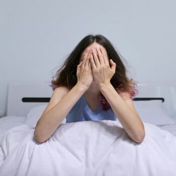 woman sitting on bed cover her face