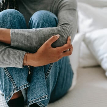 woman seated on bed hugging herself