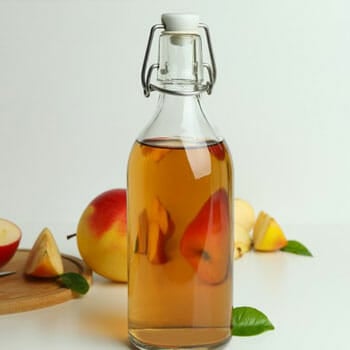apple cider in a glass bottle with fresh apple in the background