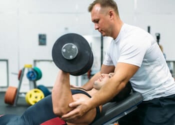 man spotting another man while lifting barbells
